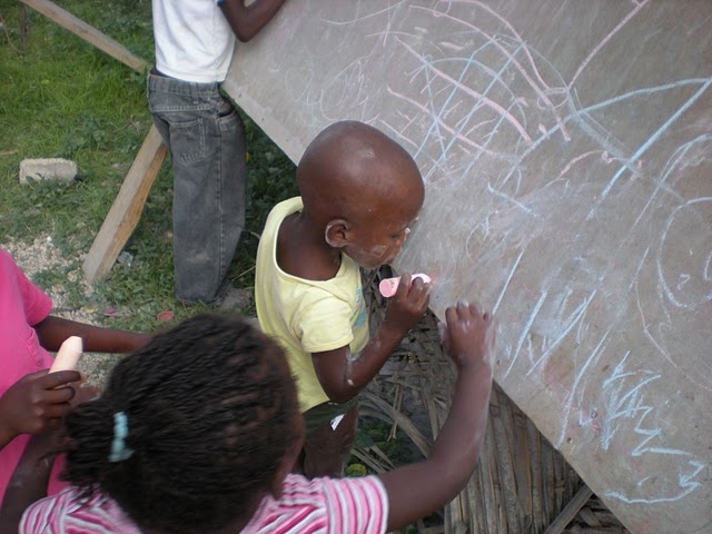 Haitian children writing on a chalkboard in an outdoor classroom.